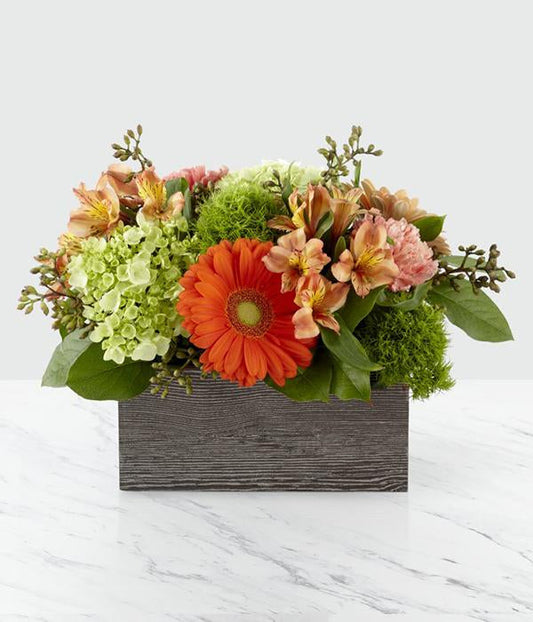 ORANGE GERBERA DAISIES, GREEN HYDRANGEAS, PEACH ALSTROMERIAS, LIGHT PINK CARNATIONS, AND GREENERY IN A WICKER BOX. STANDARD SIZE